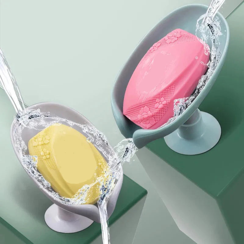 Two leaf-shaped suction cup soaps are being rinsed by water in a gray holder.