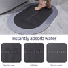 A black non-slip bath mat is shown absorbing water on a gray tiled floor.