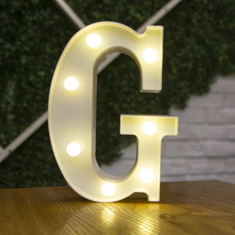 A white illuminated letter G made of LED lights resting on a wooden surface.