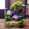 A resin water fountain featuring mossy rocks, a blue crystal, and green foliage on a wooden surface.