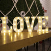 Large illuminated letters spelling LOVE made of white LED lights on a wooden surface.
