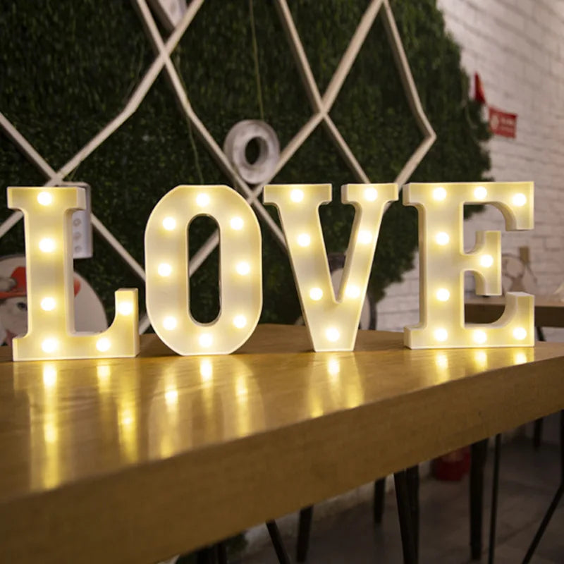 Large illuminated letters spelling LOVE made of white LED lights on a wooden surface.