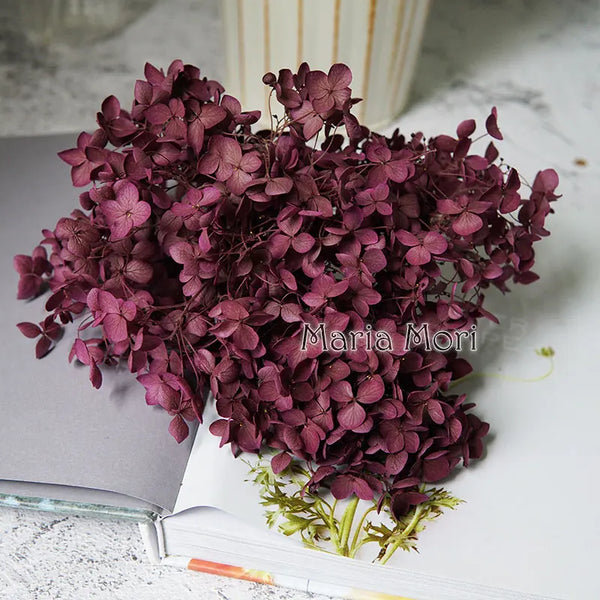 Ein Strauß tiefvioletter handgefertigter Epoxidharz-Hydrangeenblumen auf einem offenen Buch.
