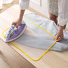 A hand is ironing a gray fabric with a purple high-temperature protection ironing cloth on a wooden surface.