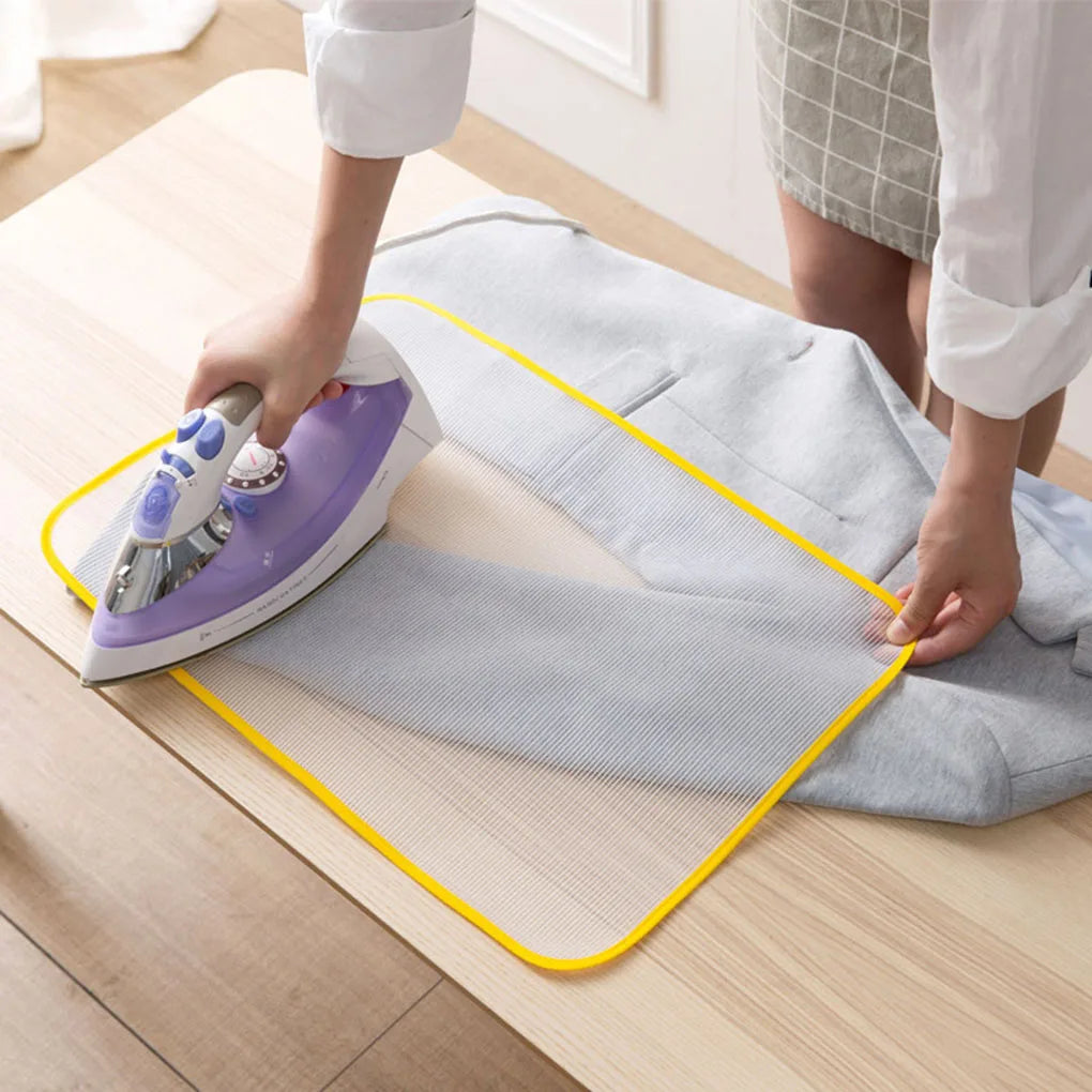 A hand is ironing a gray fabric with a purple high-temperature protection ironing cloth on a wooden surface.
