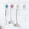 Three stainless steel silicone spatulas hanging on a white tiled wall using suction cup hooks
