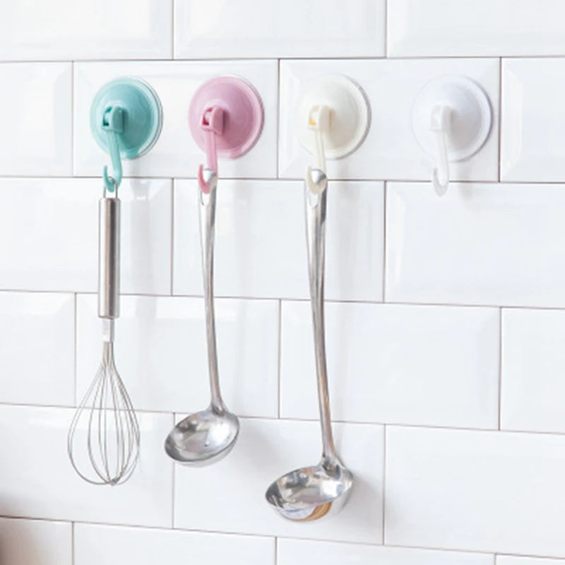 Three stainless steel silicone spatulas hanging on a white tiled wall using suction cup hooks
