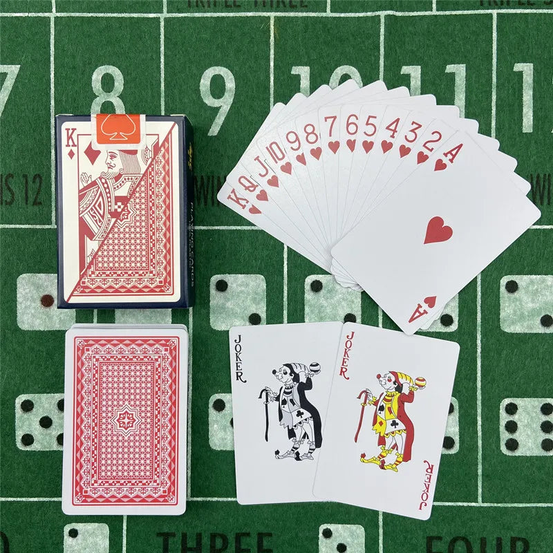 A green felt surface displays a deck of poker playing cards, including a King of Hearts, a Joker card, and several Ace-high c