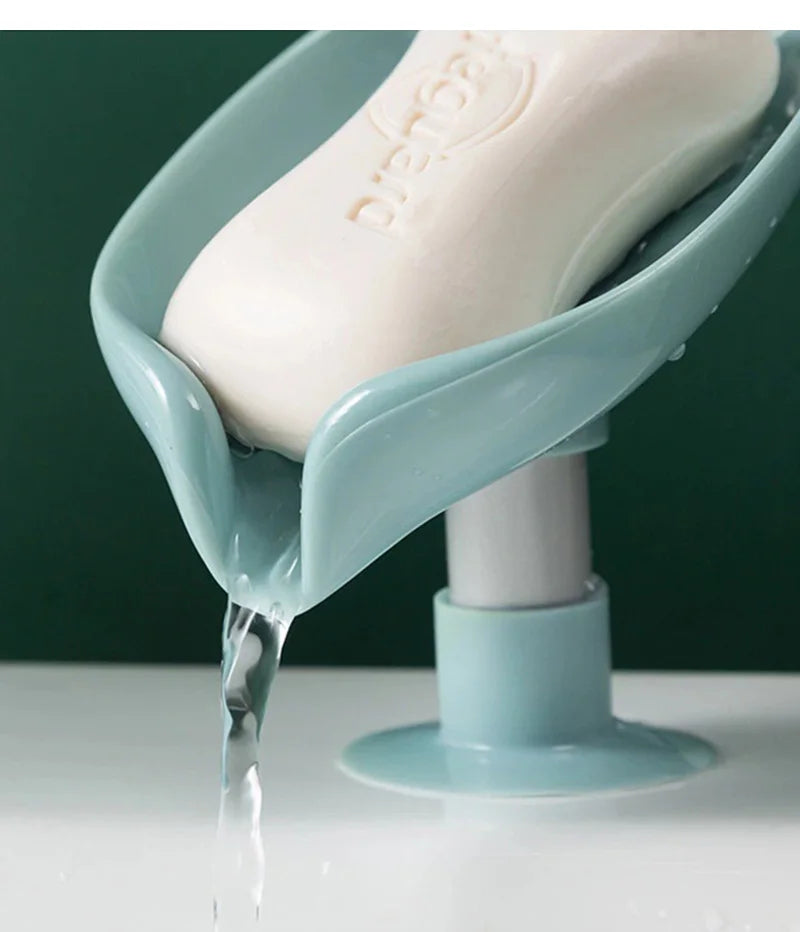 A leaf-shaped suction cup soap holder with a self-draining tray is shown dripping water onto a white surface.