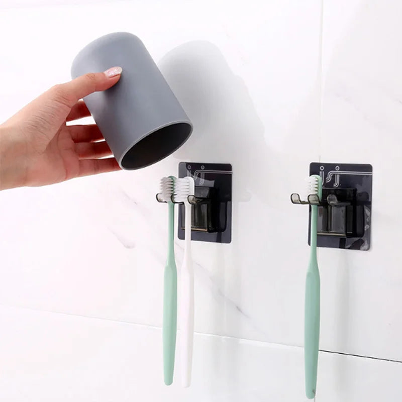 A hand holds a gray wall mounted cup and toothbrush organizer with attached toothbrushes.