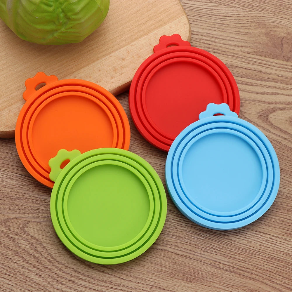 A set of colorful silicone reusable food storage lids and covers in orange, red, green, and blue on a wooden surface.