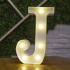 A white letter J made of LED lights standing on a wooden surface with a blurred green background.