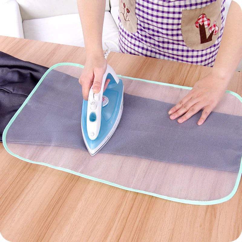 A hand is using a blue ironing tool on a mesh pad placed on a wooden table.