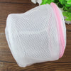 White mesh lingerie washing bag with pink trim resting on a wooden surface.