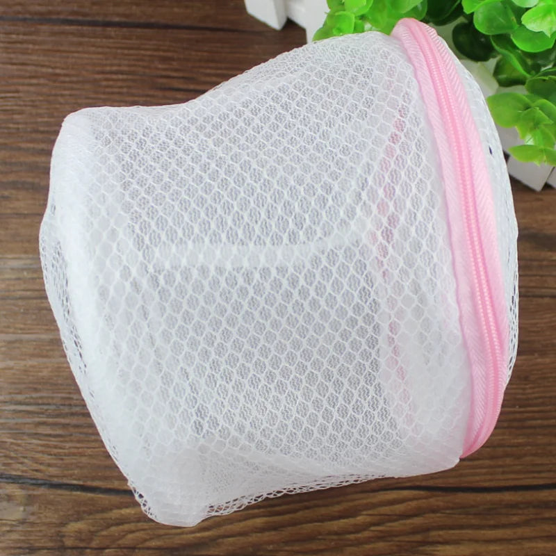 White mesh lingerie washing bag with pink trim resting on a wooden surface.