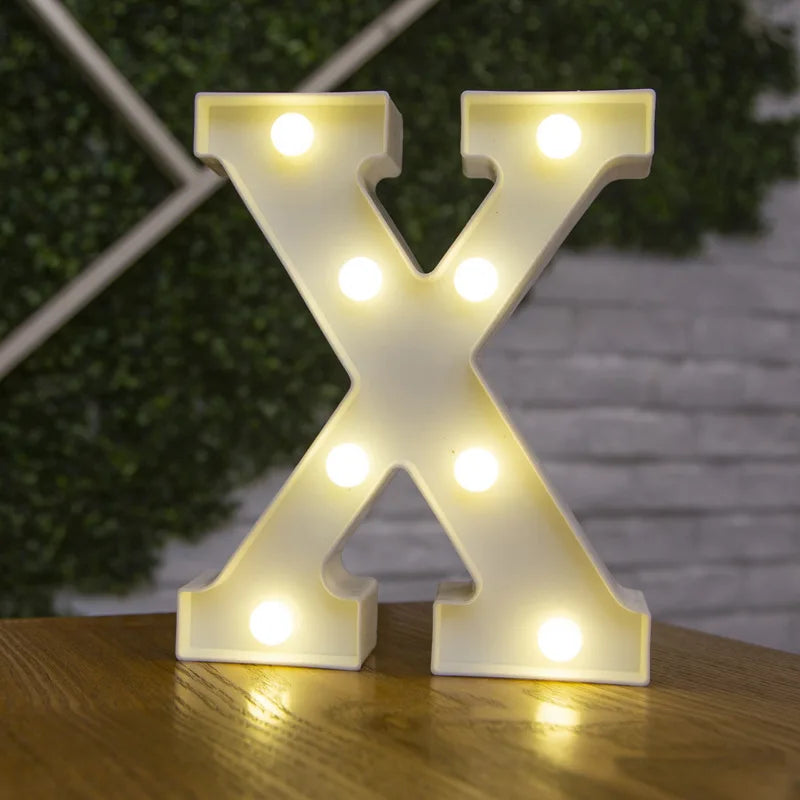 A white illuminated letter X made of LED lights resting on a wooden surface.