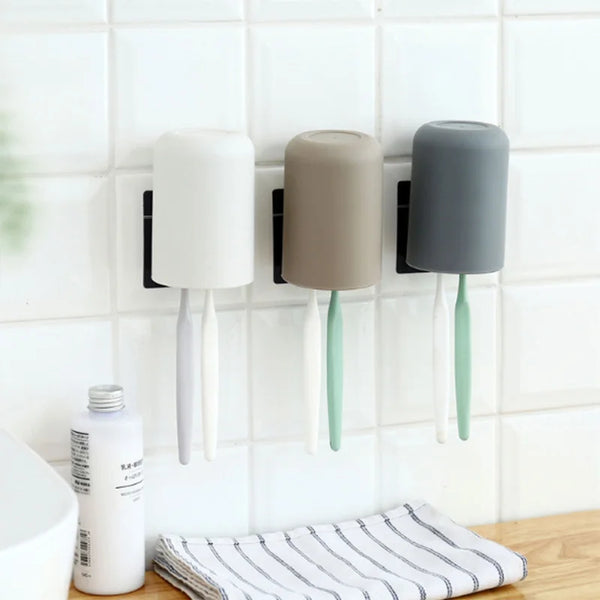 A multi-use wall mounted organizer holding three different colored cups or toothbrushes.