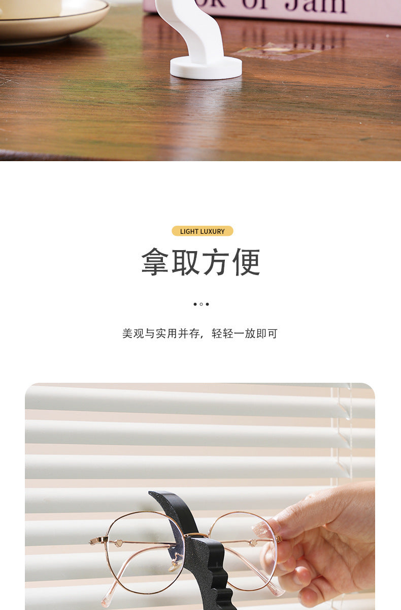 A hand is holding a pair of thin wire-frame eyeglasses on a black stand for storage.