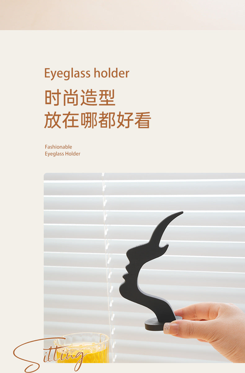 A hand holds a black 3D printed profile eyeglass holder against a white slatted background.