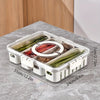 A clear plastic snack organizer tray with eight compartments holding various fresh vegetables and fruits on a gray surface.