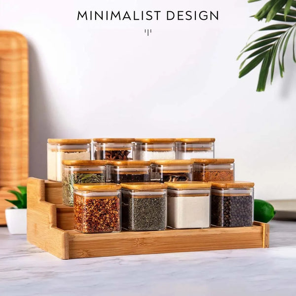 A wooden tray holds several glass spice jars with bamboo lids filled with various dried spices on a white surface.