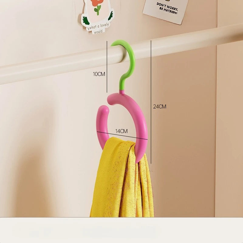 Un cintre rose avec un crochet vert est accroché sur un mur clair, à côté d'une serviette jaune.