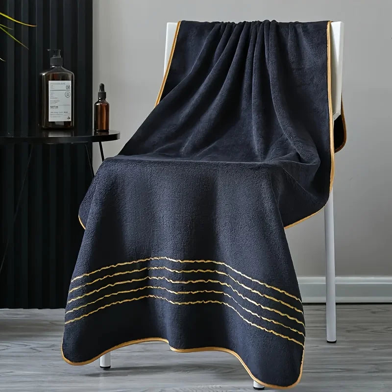 Dunkelgraues Handtuch mit goldenen Streifen, drapiert über einem weißen Ständer.