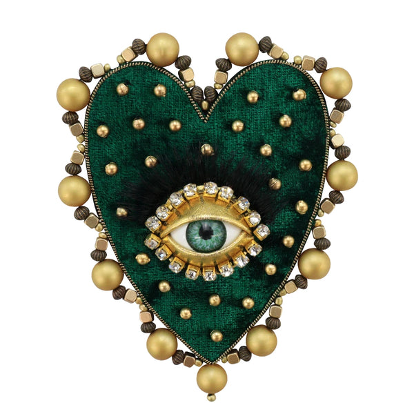 A heart-shaped appliqué featuring dark green velvet, black feathers, and a gold rhinestone eye surrounded by beaded borders.