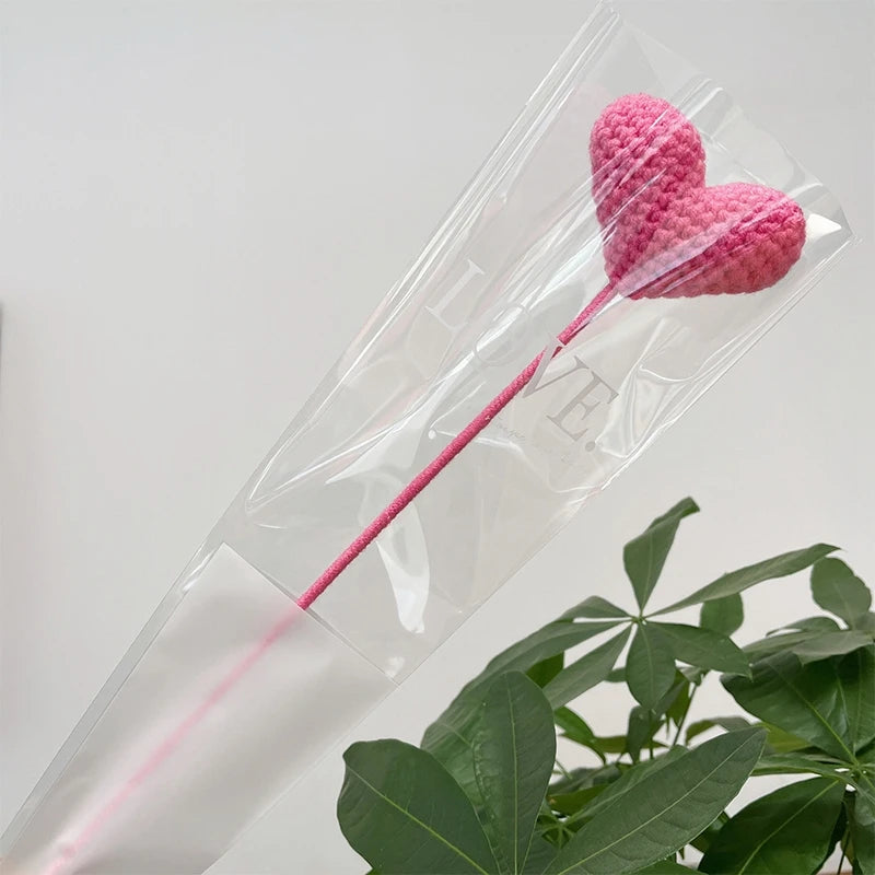 Un bouquet de cœurs roses fait à la main en coton, présenté dans une gaine transparente sur fond blanc.