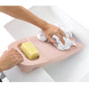 A hand is placing a bar of yellow soap onto a pink thickened washboard for delicate laundry.