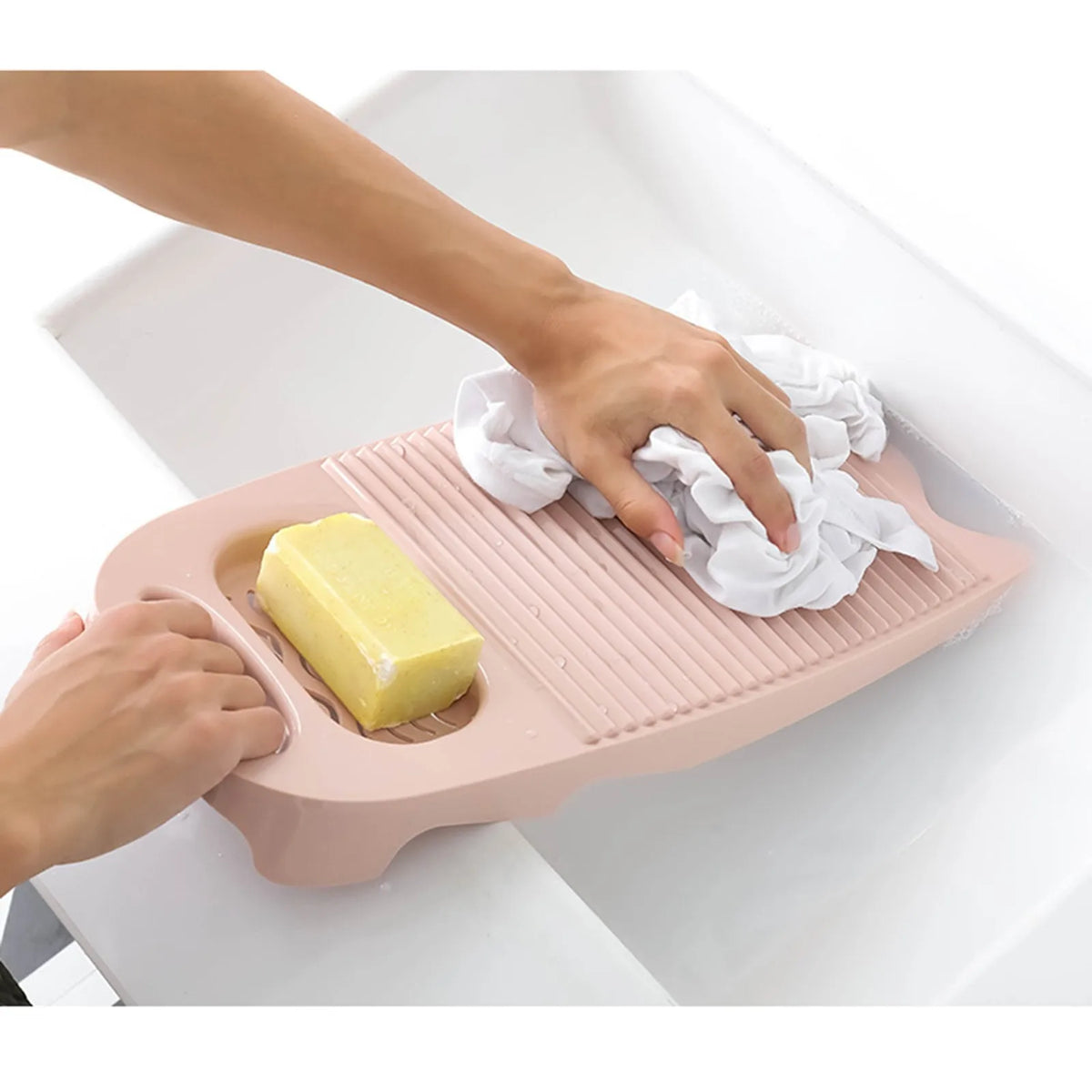 A hand is placing a bar of yellow soap onto a pink thickened washboard for delicate laundry.