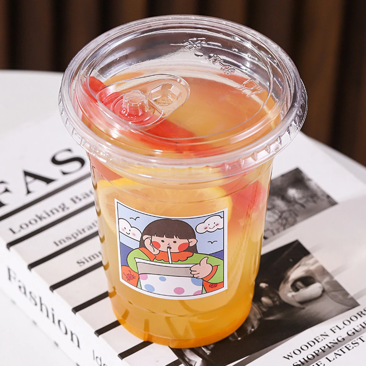 A clear plastic cup filled with orange juice or a similar beverage, resting on a magazine page.