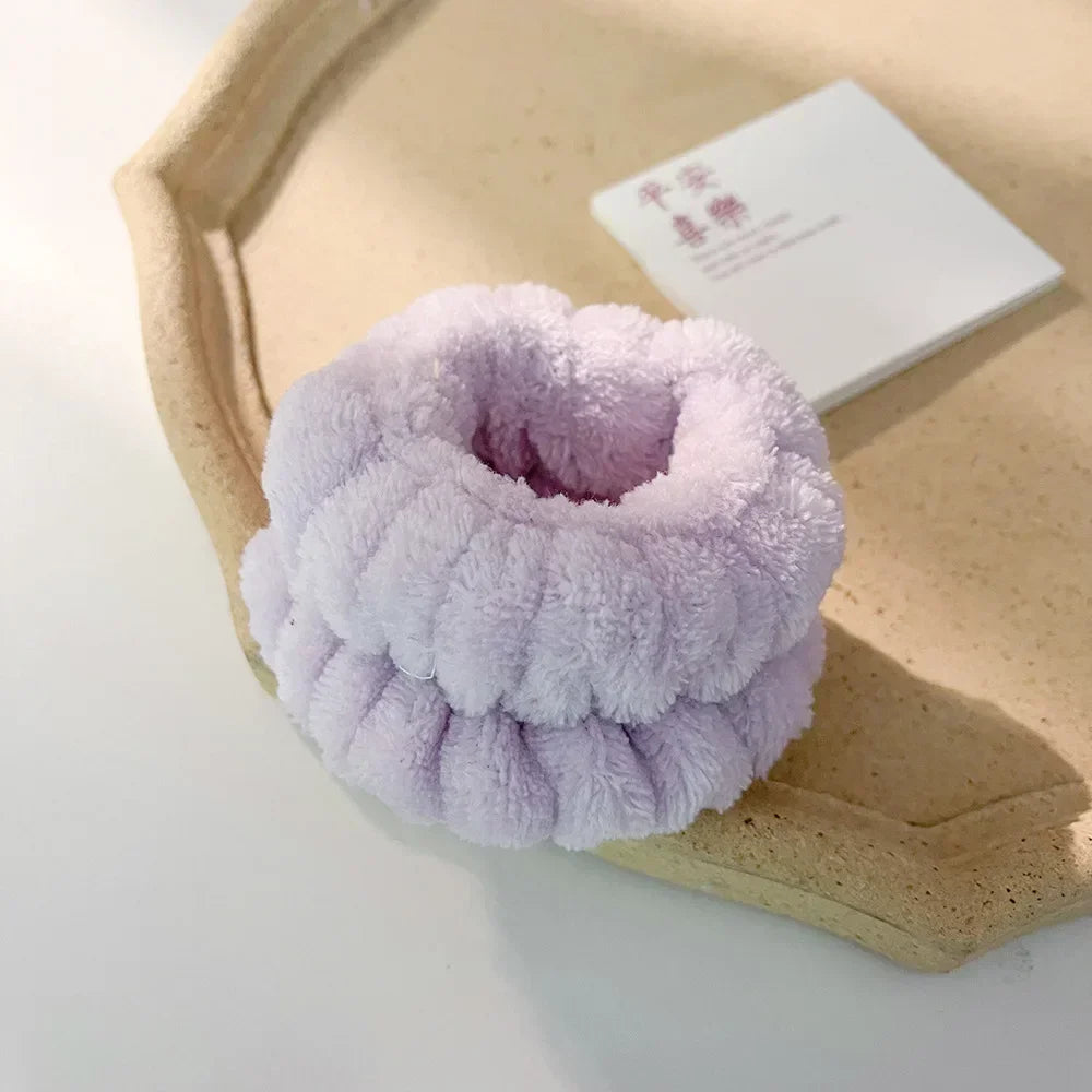 A set of purple microfiber wrist sweatbands for face washing and skincare placed on a light wooden tray.