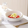A white ceramic soup bowl filled with sliced strawberries and a light yellow topping, set on a white plate.