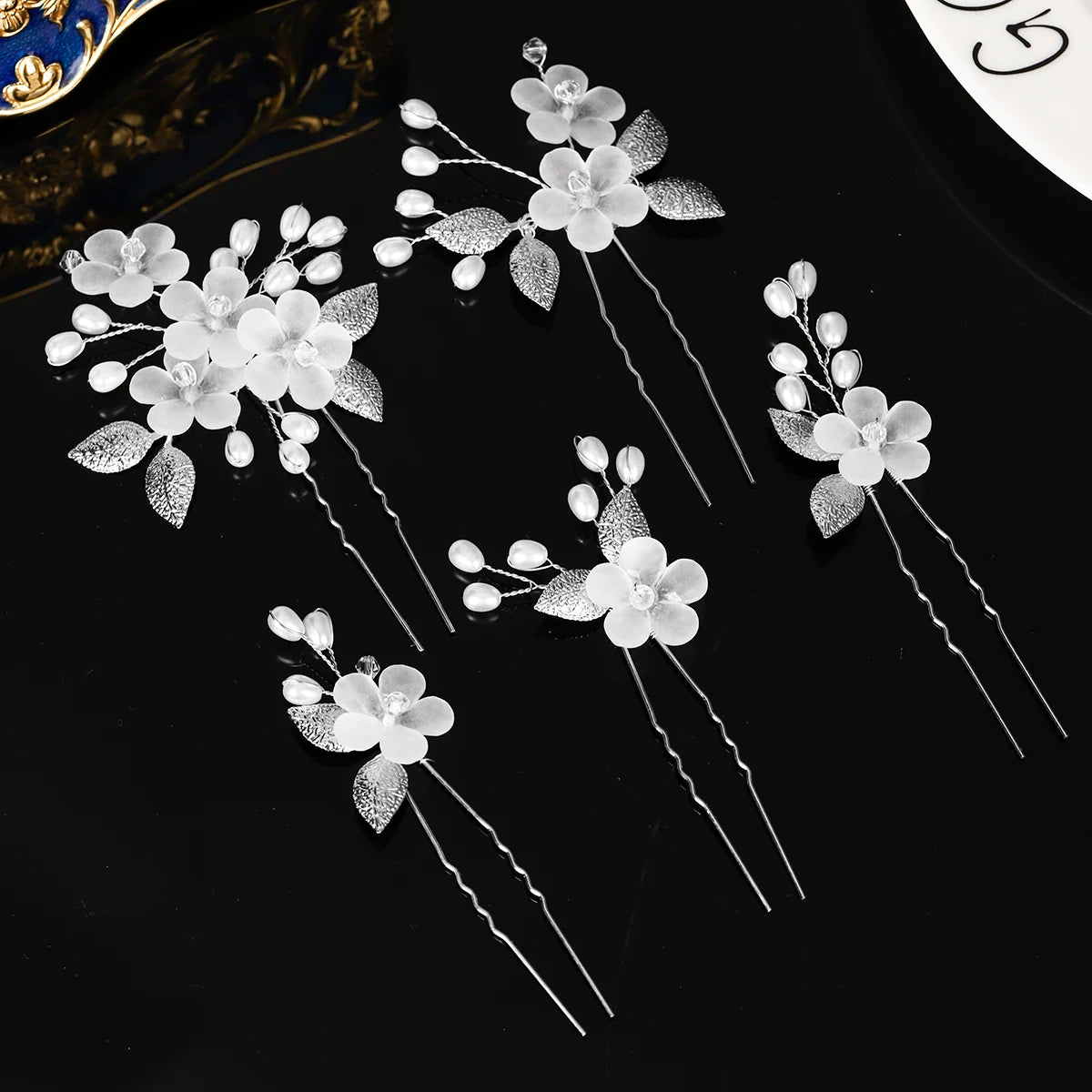 A set of delicate white pearl flower bridal hair clips with silver accents displayed on a black surface.