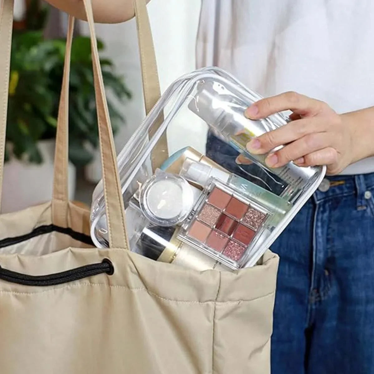Una mano sostiene una bolsa organizadora cosmética portátil transparente llena de productos de maquillaje dentro de una bolsa