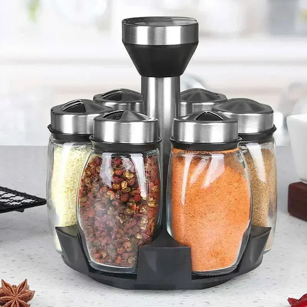 A set of rotating spice jars and seasoning dispensers in glass and metal on a black stand.