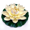 A beautiful, light yellow artificial lotus flower with white accents resting on a dark green leaf.