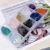 A clear plastic container holds various natural crystal stones in shades of purple, blue, green, and orange.