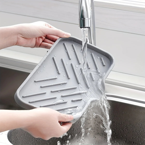 Hands are holding a silicone sink tray with drainage holes under running water in a kitchen sink.