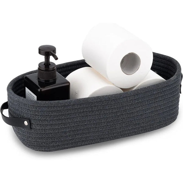 A dark gray woven cotton storage basket filled with white toilet paper rolls and a black dispenser.