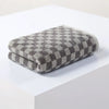 A stack of gray and white plaid cotton bath towels resting on a white surface.