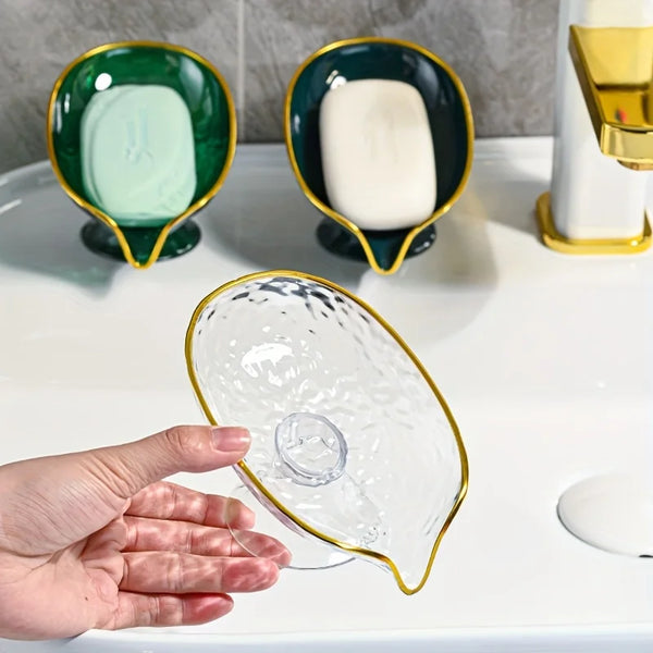 A hand is holding a clear oval plastic soap dish with drainage holes on a white surface.