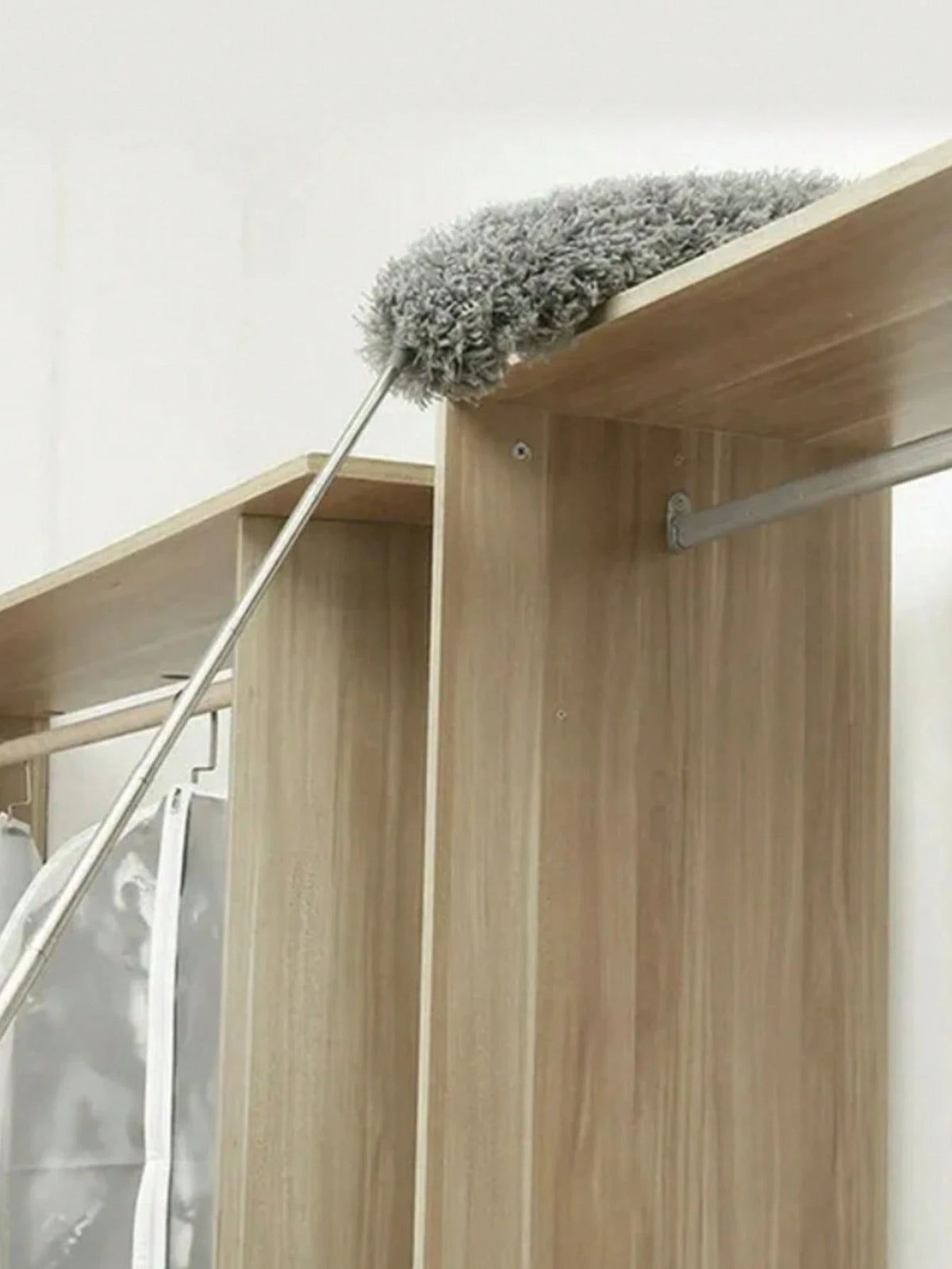 A flexible microfiber cleaning duster brush with a grey fuzzy head is shown resting on a wooden cabinet.