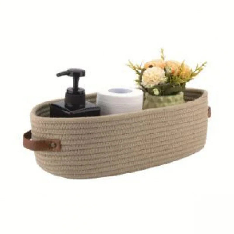 A woven cotton storage basket with a lid and a roll of paper inside, decorated with dried flowers.