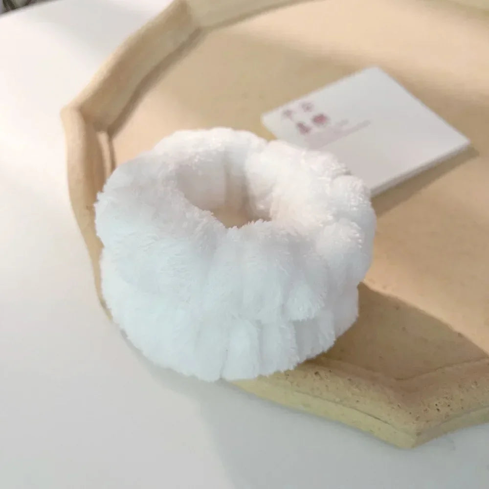 A white microfiber wrist sweatband is displayed on a light wooden tray next to a small white card.