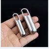 A hand holds a stainless steel travel pill box and first aid container with hinged lids.