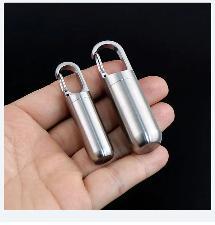 A hand holds a stainless steel travel pill box and first aid container with hinged lids.