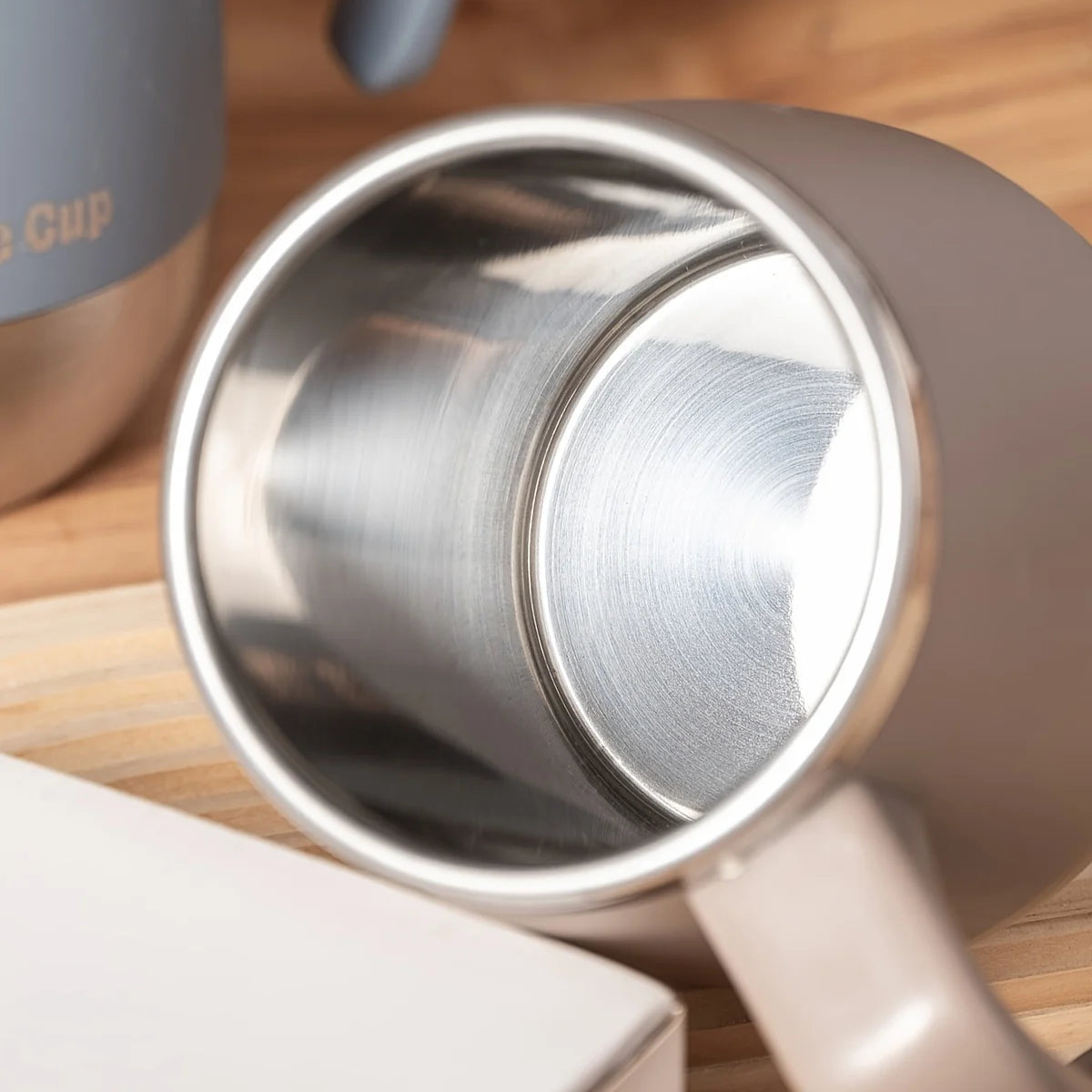 Close-up view of a stainless steel travel mug showing the interior and lid, resting on a wooden surface.