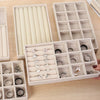 A collection of silver and gold jewelry rings and earrings organized in a light beige velvet tray with dividers.